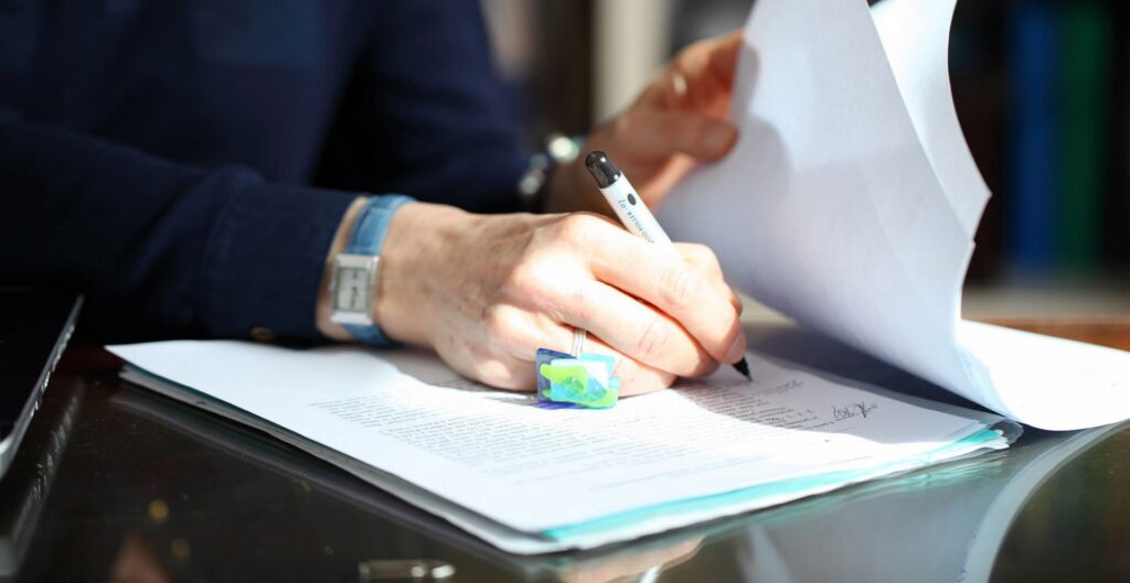 Zoom sur une main de femme, avec une bague, tenant un stylo et écrivant sur du papier