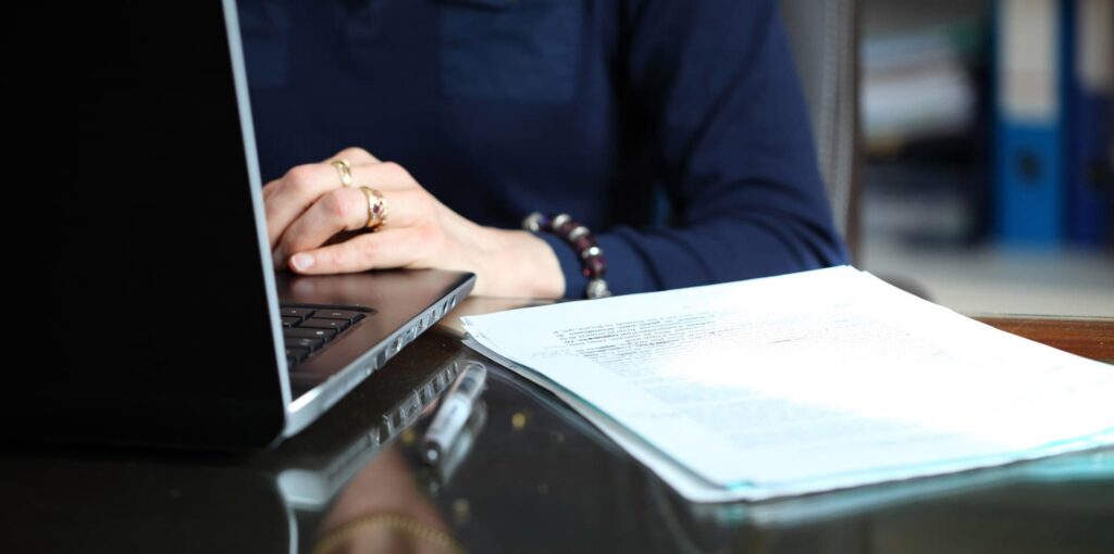 Zoom sur une main de femme retranscrivant des notes papier sur un ordinateur portable